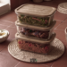 Tiled counter with stacked glass containers of jollof rice, chicken, and greens, showing meal prep for a busy schedule