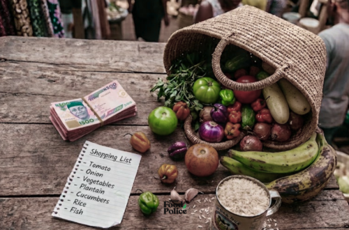 High-angle of fresh Nigerian vegetables, rice, bananas, and Naira notes on a wooden market table purchased using market hacks