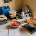 Eye-level view of an open budget notebook next to textbooks, with rice cooking, relevant to a student allowance