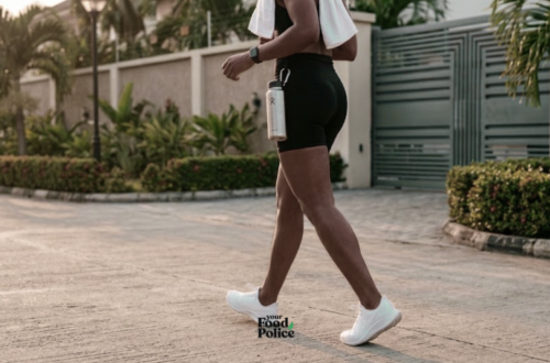 Side view of a person walking in white sneakers along a paved residential street with a water bottle