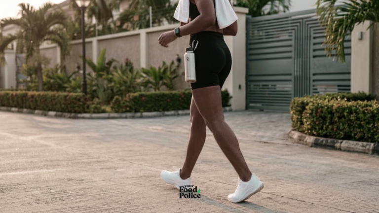 Side view of a person walking in white sneakers along a paved residential street with a water bottle