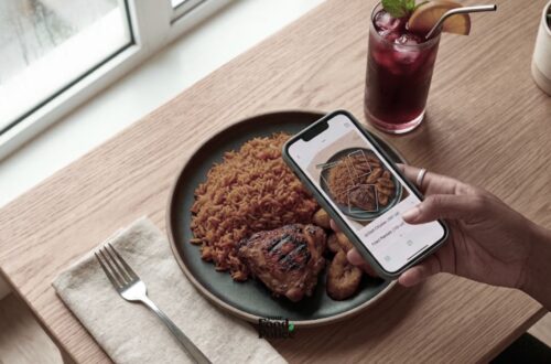 Overhead view of a phone showing an AI food tracking app identifying a plate of Jollof rice and grilled chicken.