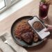 Overhead view of a phone showing an AI food tracking app identifying a plate of Jollof rice and grilled chicken.