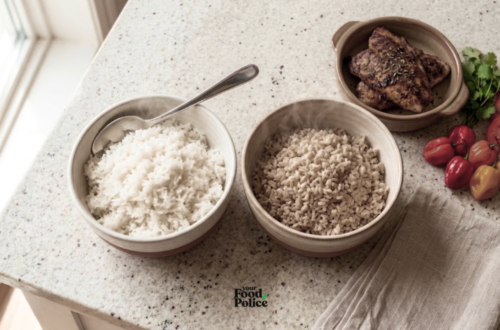 Overhead view of bowls of white and brown rice next to grilled fish and scotch bonnet peppers